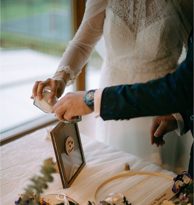 Novios realizando el ritual de la arena vertiendo arena de dos colores en un marco de madera personalizado de Arorua Bodas