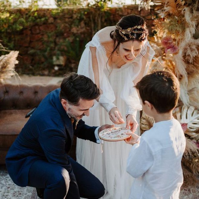 Pareja de novios y niño de arras en el momento de intercambiar los anillos en el altar con porta alianzas bastidor de Arorua Bodas