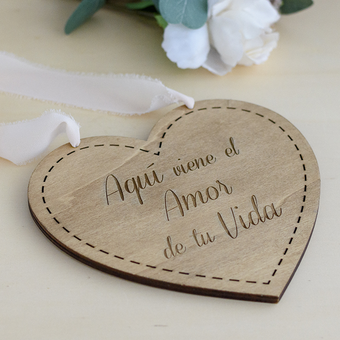 Cartel de madera para niños de arras con forma de corazón grabado con el texto aqui viene el amor de tu vida de Arorua Bodas